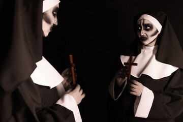 Wall Mural - Scary devilish nun with cross near mirror on black background. Halloween party look