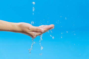 Wall Mural - Woman hand catching water on blue background