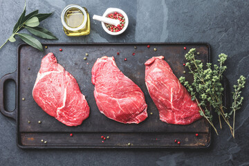 Wall Mural - Raw beef steaks with herbs and spices on cast iron frying board, top view