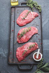 Wall Mural - Raw beef steaks with herbs and spices on cast iron frying board, top view