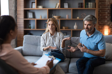 Wall Mural - Despaired mature caucasian couple arguing in clinic office interior at meeting with black psychologist