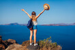 Woman traveler raised arms feeling happy looking at Caldera on Santorini island, Greece. Tourism, traveling