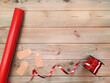 Red wrapping paper and shiny ribbon with gift tags. Copy space for text. Top view. Roll of red paper, empty tags and ribbon on wooden background. Concept of preparing Christmas gifts. Flatlay