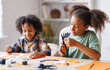 © JenkoAtaman - Happy ethnic children girl and boy making Halloween home decorations together