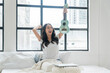 © kaew6566 - Cheerful asian woman with ukulele, laptop, pillows sitting on white bed beside window at apartment. Joyful young girl holding acoustic ukulele in morning at home. Relax female play music ukulele hobby