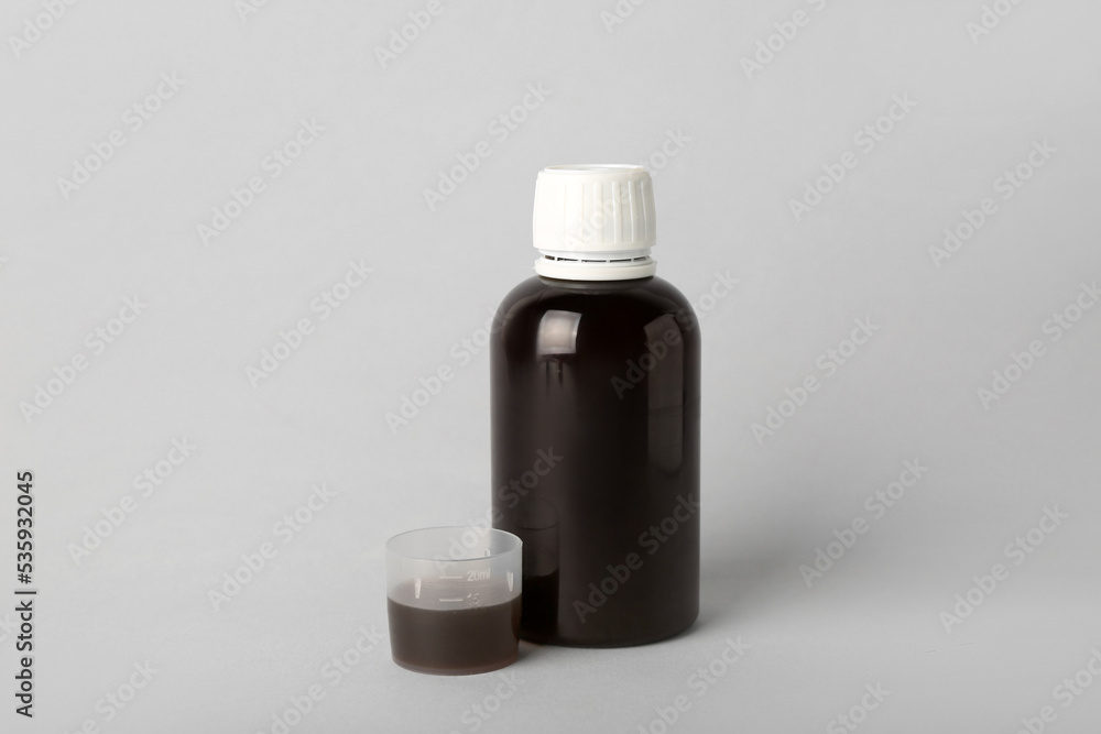 Bottle and cup of cough syrup on grey background