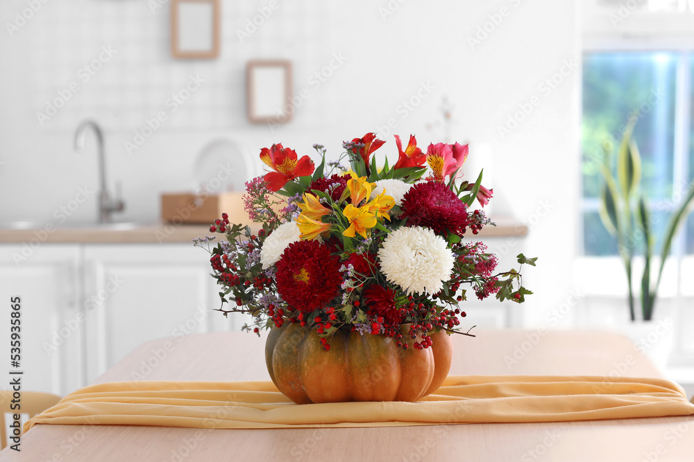 Pumpkin with autumn flowers on dining table in kitchen, closeup