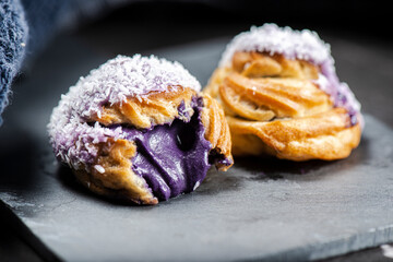 Home-made ube cream puff with purple-colored white chocolate and coconut, also known as a Profiterole.