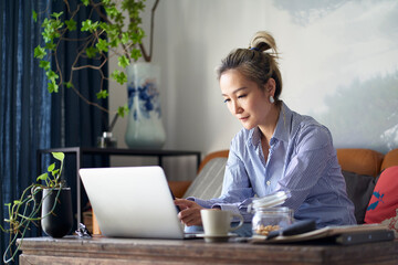 Wall Mural - mature asian woman working from home using laptop and cellphone