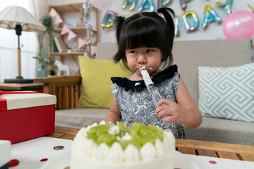 selective focus of cute naughty asian baby girl licking yummy cream on cake server during her second birthday celebration at home