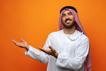 Wall Mural - Young Arab man pointing hand to copy space on orange background