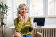 © cherryandbees - woman with headphones drinking coffee and looking at camera while sits in her room