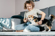 © Евгения Рубцова - Curly haired glad, cheerful barefoot woman with dog corgi. Obedience training, feeding of pet, sitting, relaxing and playing on floor in comfortable living room near sofa. Weekend leisure activity