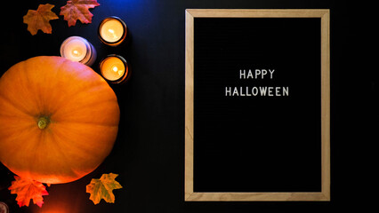 Wall Mural - Pumpkin, burning candles, autumn leaves and the inscription Happy Halloween in a wooden frame on a black background