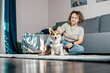 © Евгения Рубцова - Curly haired glad, cheerful barefoot woman with dog corgi sitting, relaxing and playing on floor in comfortable living room, near sofa. Active and healthy animal, healthcare. Weekend leisure activity