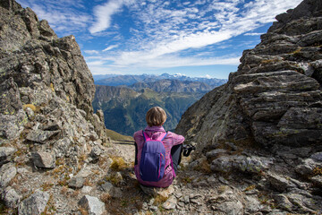 Wall Mural - The girl is sitting on the pass against the backdrop of mountain peaks. Beautiful mountain landscape for recreation, travel and a healthy lifestyle. On the back plan is the summit of Elbrus. Caucasus,