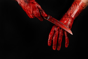 Fototapeta a man wipes a bloody knife with his hand on a black background. 