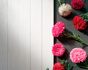 Wall Mural - Chaotically scattered aster flowers are on a dark rough background next to an empty white wooden table. Abstract floral autumn composition with copy space.