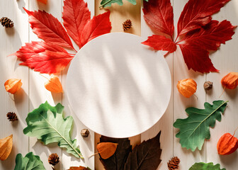 Wall Mural - A round paper frame is above yellow, red, green fallen leaves and physalis flowers on a white wooden background. Autumn, fall, thanksgiving day concept. Flat lay. Top view. Copy space.