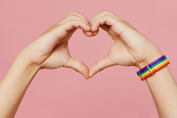 Wall Mural - Close up cropped gay male hand with bracelet show shape heart with hands heart-shape sign isolated on pastel plain light pink background. Lifestyle lgbtq pride concept. Copy space advertising mock up.