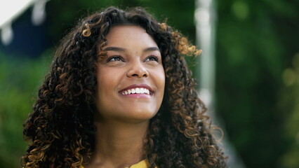 Hopeful young woman looking at sky with FAITH. One happy African American person closeup face standing outdoors