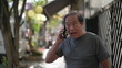 © Marco - Happy senior man using cellphone standing outdoors in city street. Portrait older Asian American person typing message on smartphone device smiling