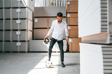 Wall Mural - Taking a break, playing with soccer ball. Storage worker is in the warehouse with bunch of products