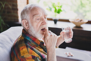 Sticker - Photo of upset unhappy retired man dressed plaid shirt sitting couch drinking medicines water indoors apartment