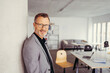 © contrastwerkstatt - Smiling attractive mature man wearing glasses in modern office with copy space looking at the camera