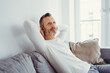 © contrastwerkstatt - Happy man enjoying a blissful rest sitting on a comfortable sofa clasping his hands behind his neck with his eyes closed and a pleased smile , side view