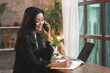 © Wasaphol - Professional Asian businesswoman using a laptop computer working in cyberspace online, she drinking coffee and working in the co-working space, talking on the phone and taking notes in the notebook.