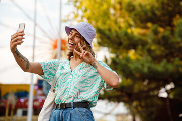 Young blonde woman wearing panama using mobile phone in attraction park