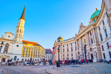 Wall Mural - Evening on Michaelerplatz with lines of tourist horse-drawn carriages at Hofburg Palace in Vienna, Austria