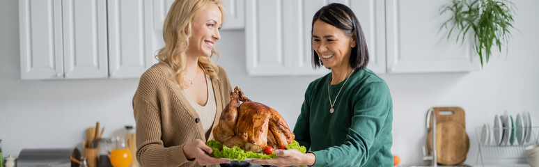 Wall Mural - Multiethnic woman holding thanksgiving turkey with daughter at home, banner