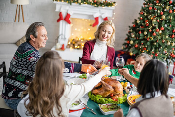 Wall Mural - cheerful interracial family clinking glasses near delicious roasted turkey on christmas dinner at home