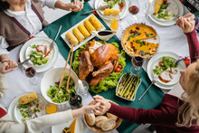 Top View Of Interracial Family Holding Hands While Praying Near Tasty Meal Served For Thanksgiving Celebration