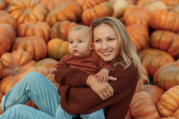 A young beautiful woman with a baby in her arms near orange pumpkins