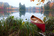 Red wood canoe on shore of a small lake with an island on a cloudy autumn morning