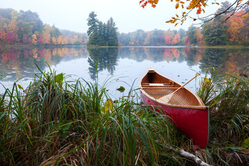 Wall Mural - red wood canoe on shore of a small lake with an island on a cloudy autumn morning