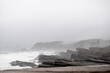 Paisaje de la costa rocosa con rocas metamórficas mirando al mar con espuma y niebla húmeda de la costa en ascenso hacia el bosque de fondo en día de lluvia y nubes en ambiente frío al sur de chile