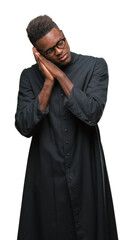 Canvas Print - Young african american priest man over isolated background sleeping tired dreaming and posing with hands together while smiling with closed eyes.