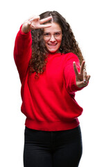 Sticker - Beautiful brunette curly hair young girl wearing glasses and winter sweater over isolated background smiling looking to the camera showing fingers doing victory sign. Number two.