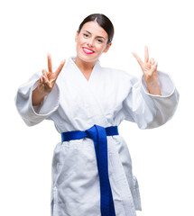 Poster - Young beautiful woman wearing karate kimono uniform over isolated background smiling looking to the camera showing fingers doing victory sign. Number two.