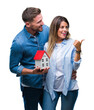 © Krakenimages.com - Young couple in love holding house over isolated background pointing and showing with thumb up to the side with happy face smiling