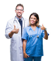 Wall Mural - Young couple of doctor and surgeon over isolated background doing happy thumbs up gesture with hand. Approving expression looking at the camera with showing success.