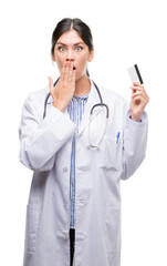 Sticker - Young hispanic doctor woman holding credit card cover mouth with hand shocked with shame for mistake, expression of fear, scared in silence, secret concept