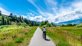 Fototapeta Las - Woman on an e-bike on the trail along the Okangen River Canal between Oliver and Osoyoos in the Okanagen Valley of British Columbia,  Canada