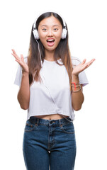 Poster - Young asian woman listening to music wearing headphones isolated background very happy and excited, winner expression celebrating victory screaming with big smile and raised hands