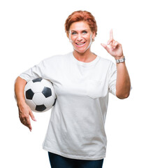 Canvas Print - Atrractive senior caucasian redhead woman holding soccer ball over isolated background surprised with an idea or question pointing finger with happy face, number one