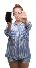 Poster - Young blonde woman using smartphone with open hand doing stop sign with serious and confident expression, defense gesture